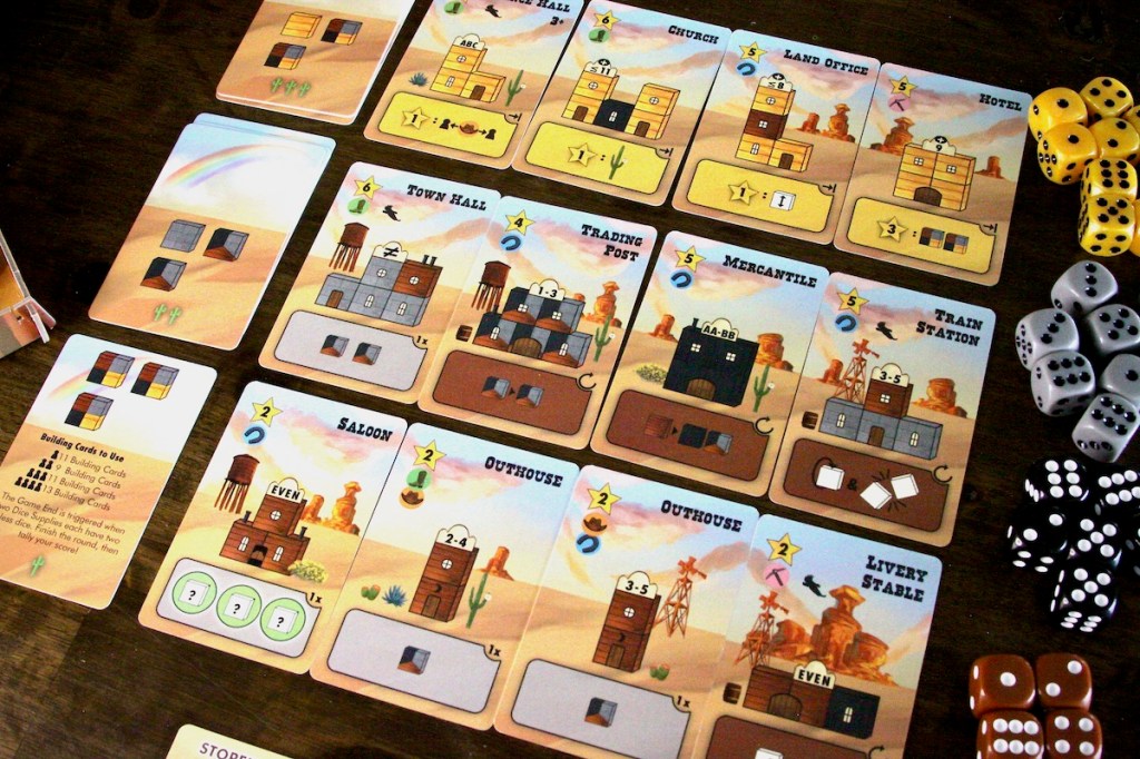 The building card market featuring an outhouse, saloon, mercantile, town hall, and hotel in Tumble Town board game by Weird Giraffe Games