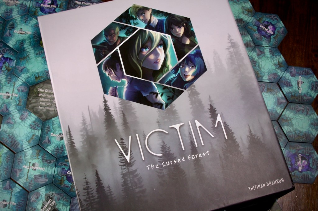 Victim the Cursed Forest Board Game Box Cover on top of forest tiles