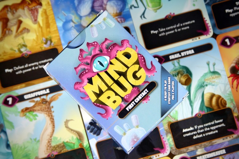 mindbug first contact box cover with cards in the background; card game designed by Richard Garfield

